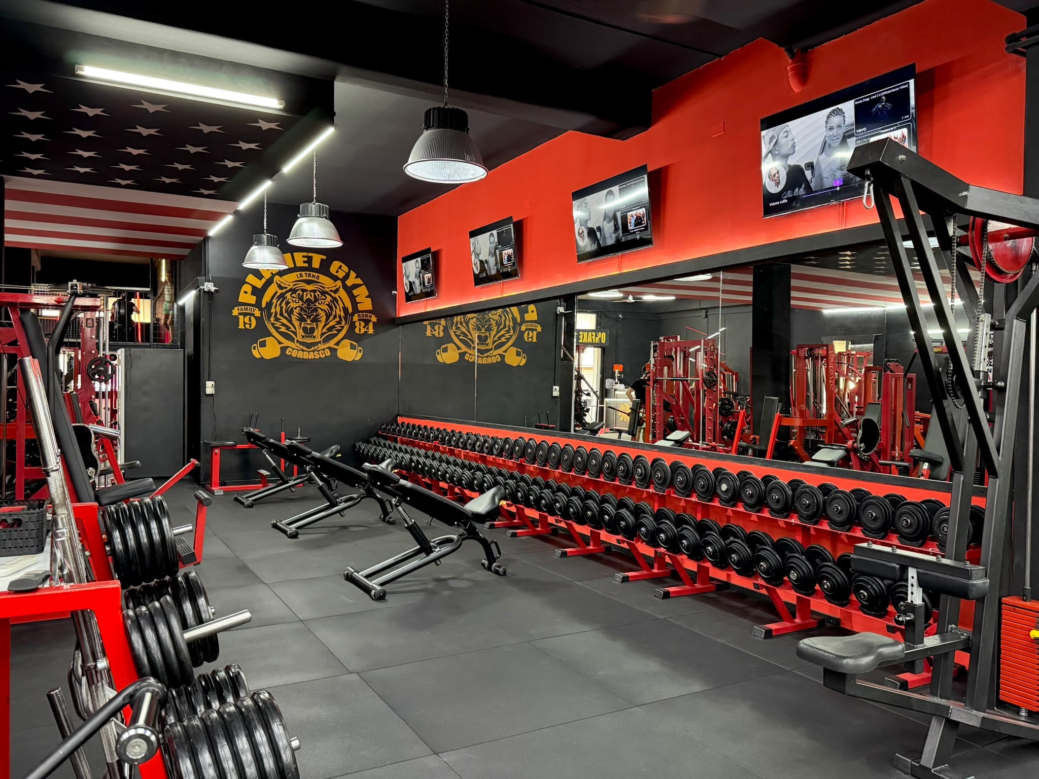 Planet Gym — sala pesi rossa e nera con rastrelliera di manubri